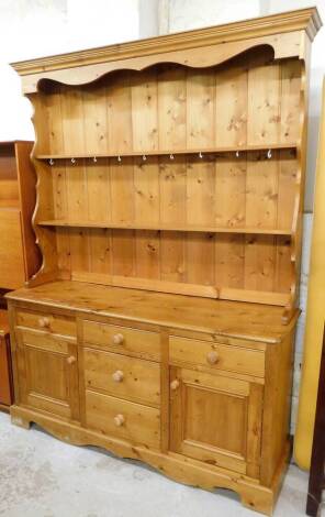 A pine kitchen dresser, the moulded top with plate rack section and two shelves, on a sideboard base, with arrangement of single drawer and door to each side and three drawers to centre, each on knop handles, 206cm high overall, 152cm wide, 46cm deep.