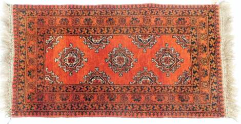 A Persian style wool rug, in orange, cream and black, with three central motifs and four varied borders, on tassel ends, fabric label to back no. 00139, 137cm x 74cm.