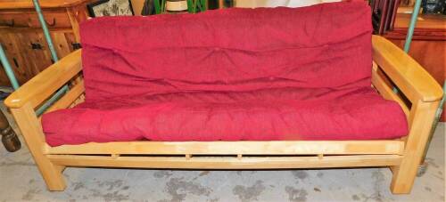 A pine framed sofa bed, with red upholstered seat and drop down back, 90cm high, 219cm wide, 92cm deep.