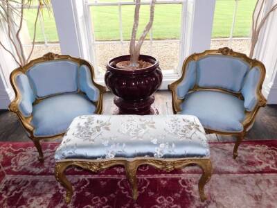 A pair of Louis XV style French gilt wood and gesso fauteuils, each with a moulded show frame, carved with scrolls, shell, etc., upholstered in blue patterned fabric, on cabriole legs and a Louis XV style French rectangular stool, with a padded seat uphol