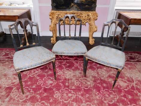 A set of three George III painted side chairs, each decorated in gilt with swags, patera, etc, on a black ground, with a pierced rail back, blue upholstered and padded feet on square tapering legs.