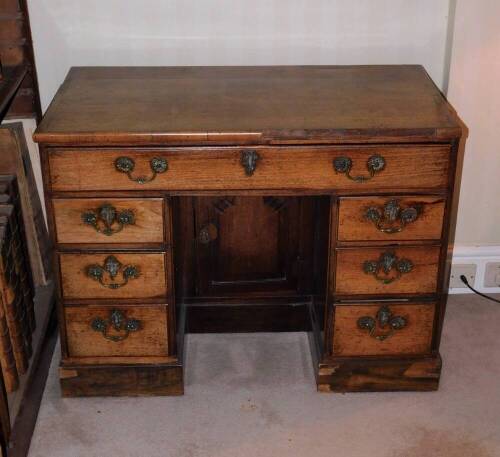 A George III mahogany kneehole desk, the top with a moulded edge above a frieze drawer and flanked by six small drawers, each with cast brass handles around a central panelled door on a plinth base, 74cm high, 96cm wide, 50cm deep.