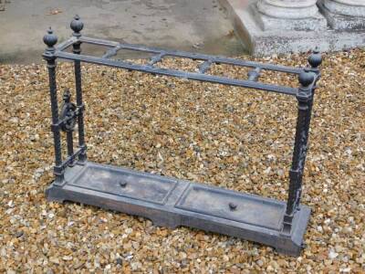 A Victorian cast iron umbrella stand, with five divisions, on spiral end supports, headed by loaded finials, the rectangular base with two dished drip trays, each with a central handle, on bracket feet, 69cm high, 98cm wide.