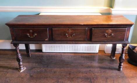 An early 18thC oak dresser base, the top with a moulded edge above three frieze drawers each with drop brass handles, on turned front legs 83cm high, 176cm wide, 47cm deep. (AF)