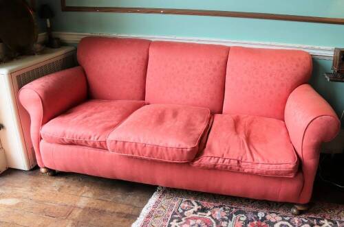 An Edwardian three seater sofa, re-upholstered in pink damask fabric, on bun feet with castors, 201cm wide.