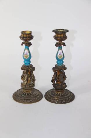 A pair of late 19thC ormolu figural candlesticks, with urn shaped sconces (one lacking) and holders with porcelain baluster columns, painted with reserves of flowers, on a blue ground, raised above three standing putti, on stepped circular bases with acan