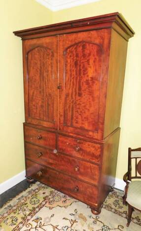 A Victorian mahogany clothes press, the top with a moulded cornice above two arched panelled doors enclosing a later fitted clothes rail, the base with two short and two long drawers, on bun feet, 212cm high, 232cm wide.