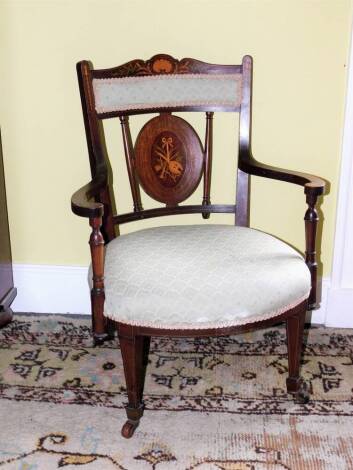 An Edwardian mahogany and marquetry open armchair, with a padded back and seat inlaid with musical trophies, shells, flowers, etc., on square tapering legs with ceramic castors.