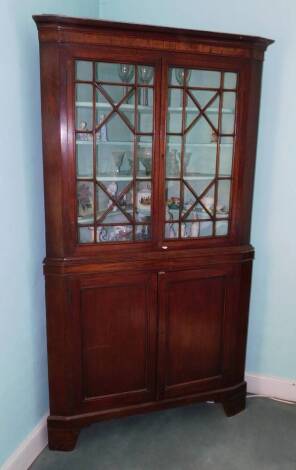 An early 19thC mahogany freestanding corner cabinet, with a moulded cornice and an ebony boxwood strung crossbanded frieze above two astragal glazed doors enclosing a painted interior, the base with two panelled doors on bracket feet, 207cm high, 112cm wi