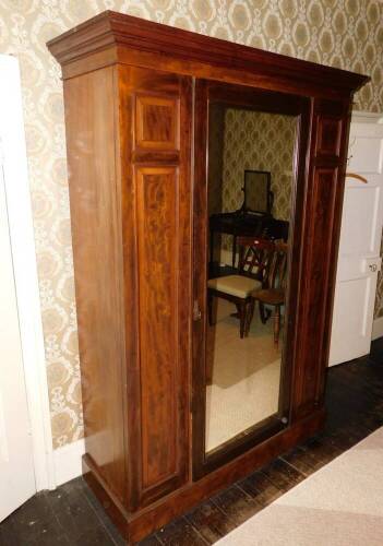 A late Victorian mahogany wardrobe, with a moulded cornice above a single mirrored door flanked by two panels on a plinth base, 225cm high, 144cm wide, 52cm deep.