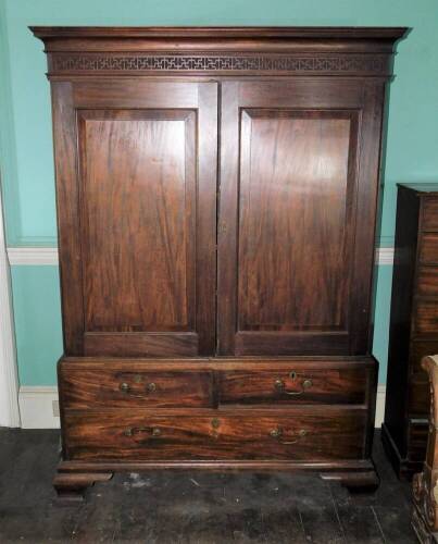 A George III mahogany clothes press, the top with moulded cornice above a blind fret carved frieze, two panelled doors enclosing sliding trays the base with two short and one long drawer on ogee bracket feet, 117cm high, 126cm wide, 61cm deep.