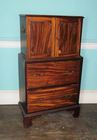 A George III mahogany collector's cabinet, the top with a moulded edge, above two panelled doors, flanked by side handles, enclosing an arrangement of two short and five long drawers, each with ring handles, the base with two deep drawers with brass drop 