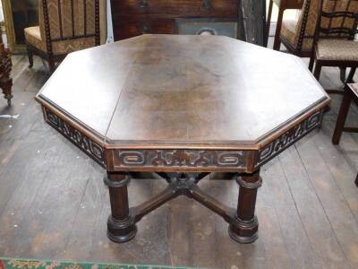 A Victorian Gothic oak library table, the octagonal planked top with a moulded edge above an arrangement of four drawers and four false drawers, each carved with scrolls, etc., on four octagonal supports, joined by an X shaped stretcher, with loped pater