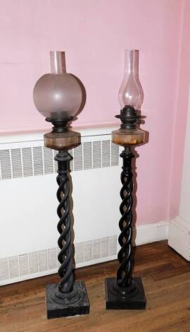 A pair of ebonised open barley twist column lamp standards, housing a clear glass reservoir oil lamp, column height 74cm. (the illustrated broken globe is no longer part of the lot)