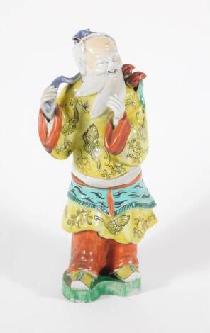 A 19thC Chinese polychrome porcelain figure of a bearded sage, dressed in a yellow robe, 27cm high.