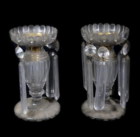 A pair of Regency cut glass lustre candlesticks, with brass stems and holders, and cut petalated drip pans, with slice and ring cut neck and fluted baluster stems, raised upon stepped circular bases and cut feet, lacking some lustre drops, 19cm high.