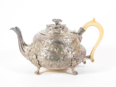 A William IV silver teapot, of circular bombe form, the domed hinged lid with a flower head knop, the body with repousse scroll and flower head decoration, and an ivory query handle, with a leaf capped spout, raised on four mask head rococo scroll feet, L