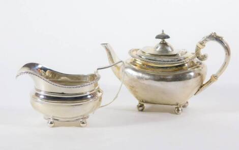 A late Victorian silver teapot, with swollen tapered body and flanged gadrooned border, leaf capped query handle and raised on four ball feet, London 1899 and a crested George IV silver cream jug of similar design, London 1820, 15.5oz all in.