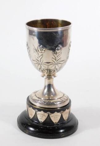 A Victorian silver prize cup, of goblet shape embossed with flowers and foliage above feather lappets, tapered circular foot, London 1848, makers RS crowned, and the socle base with winners shields, 18cm high, 12.59oz.