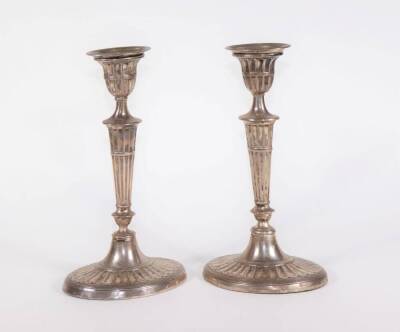 A pair of Edwardian silver Adam style candlesticks, with oval reeded sconces and urn shaped holders, on slender tapered and fluted baluster columns and oval fluted bases with reeded borders, London 1906, with filled bases, 21.5cm high.