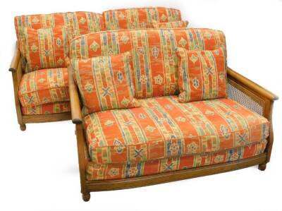 An Ercol elm and caned three seater sofa, and a matching two seat sofa, with geometric multicoloured fabric on bun feet.