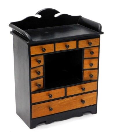 A small ebonised and mahogany table top cabinet, with a raised back and various drawers, each with brown Bakelite handles on bracket feet, 58cm high, 43cm wide.