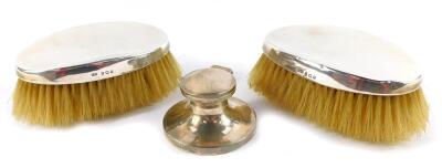 A pair of Edward VII silver backed hair brushes, Birmingham 1910, together with a George V silver ink well, of capstan form, with clear glass liner, Birmingham 1915. (3)