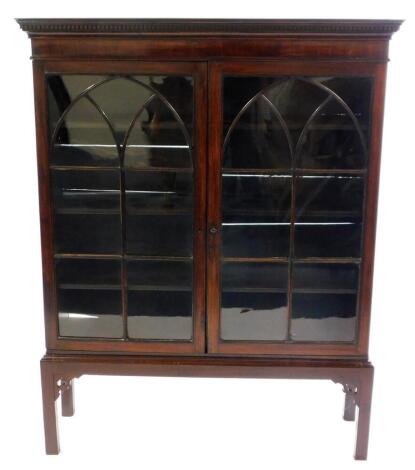 A George III mahogany bookcase on stand, the outswept pediment with dentil moulding over two glazed doors, with arched tracery, opening to reveal three shelves, raised on a base with rectangular block feet, with key, 152cm high, 120cm wide, 33cm deep.