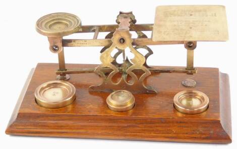 A set of early 20thC brass postal scales, with weights, raised on an oak base, 31.5cm wide.