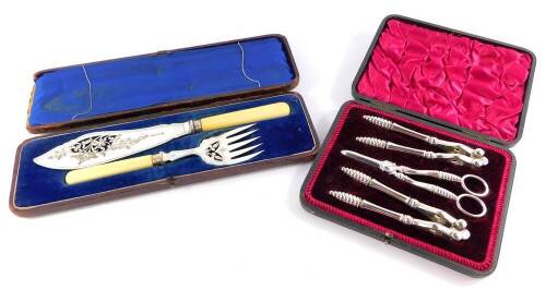 A set of early 20thC silver plated dessert implements, cased, comprising two pairs of nut crackers and a pair of grape scissors, together with a pair of silver plate and ivory handled fish servers, cased. (2)