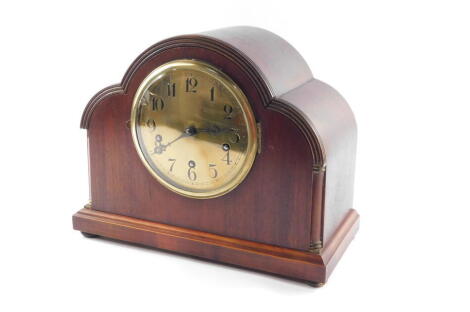 An Edwardian mahogany cased mantel clock, the circular brass dial bearing Arabic numerals, Continental movement with Westminster chimes, the case of architectural cloud form, raised on a plinth base on bun feet, with key, 29cm high, 36cm wide.