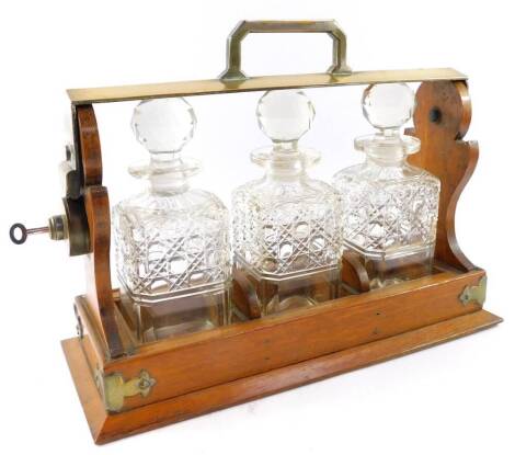 An oak and plated three bottle tantalus, worn, containing cut glass decanters and stoppers, with key, 29.5cm high, 39cm wide.