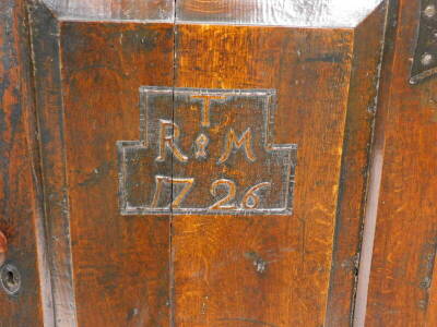 An early 18thC joined oak livery cupboard, the loose top with a moulded edge above a single panelled door bearing initials T above R&M and date 1726, flanked to one side with three panels, enclosing two shelves, on end supports, 117cm high, 110cm wide, 51 - 2