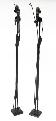 A pair of African bronze tribal sculptures, each of an elongated man with beard and walking stick, on a square tapered base, 66cm high, 6cm wide. (2)