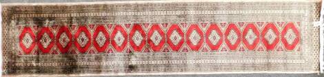 An Afghan type runner, with fifteen central red medallions, with five bordered design, in taupe and orange with white tassel ends, 372cm long x 84cm wide.