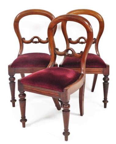 A set of three Victorian balloon back dining chairs, with mahogany backs on a curved top with pierced central splat, on turned splayed legs, with drop in red velvet seats, 92cm high, seat 39cm deep. (3)