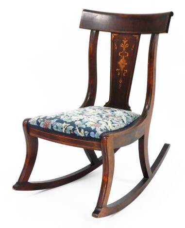 An Edwardian mahogany inlaid rocking chair, the back splat with marquetry inlay with mother of pearl centre, on two shaped supports and a tapestry upholstered seat, 83cm high, 78cm deep, 56cm wide.