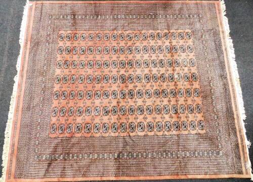 A Pakistani Bokhara carpet, the central rectangular panel set with medallions on a diamond shaped and medallion border, on a pink ground, with tassel ends, 250cm x 284cm.