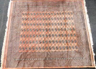 A Pakistani Bokhara carpet, the central rectangular panel set with medallions on a diamond shaped and medallion border, on a pink ground, with tassel ends, 250cm x 284cm.