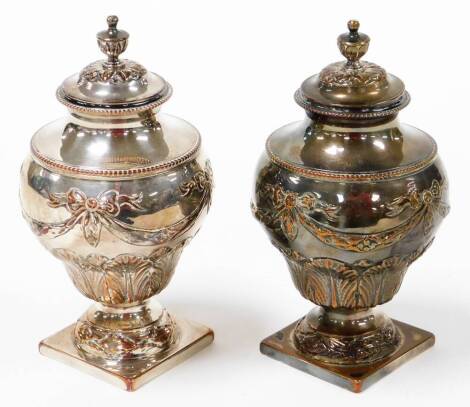 A pair of old Sheffield plate tea caddies, each shaped as an urn, with bow and scroll decoration, on square bases with finials, possibly c. 1790, 18cm high. (2)