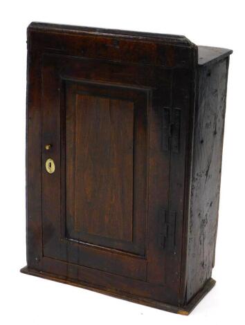 A late 17th/early 18thC oak wall cupboard, the top with a moulded edge above a single panelled door, with iron H shaped hinges, 68cm high, 47cm wide, 23cm deep.