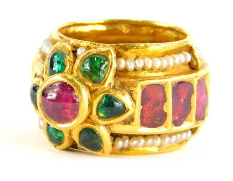 An Indian dress ring, set with various cabochon cut rubies, emeralds and seed pearls, the centre cluster in raised setting, the band set with various rough cut rubies, on a seed pearl surround, yellow metal, unmarked, ring size L, 12.1g all in.