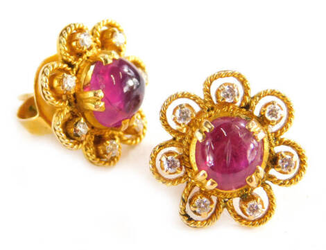 A pair of ruby and diamond cluster earrings, each set with central cabochon cut ruby with seven point flower surround, in rope twist design border, on a screw on butterfly back, yellow metal, the backs marked 18kt, earring head 1.4cm wide, 7.6g all in.