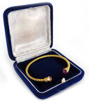 A torc bangle, the bangle ends set with cabochon cut ruby, and diamond surround, on a spiral turned bracelet, yellow metal, unmarked, 6cm wide, 16.3g all in.