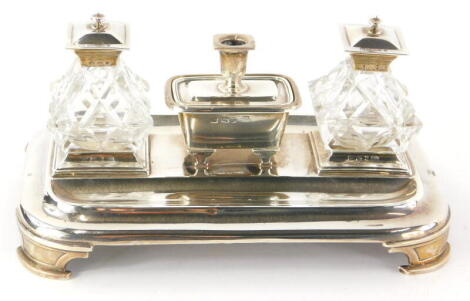 A Victorian silver ink stand, of rectangular form, with two pen recesses, and a central ink well flanked by two cut glass ink wells with silver mounts and hinged lids, Sheffield 1842 and 1843, weighable silver, 15½oz, 22.5cm wide.