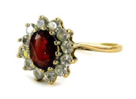 A 9ct gold floral cluster ring, the central garnet surrounded by various CZ stones, in a claw setting, on pierced design shoulders, ring size U, 2.8g all in.