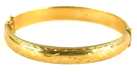 A 9ct gold hinged bangle, the top with scroll engraved design on a plain base, with safety chain, 6cm diameter, 9.9g all in.