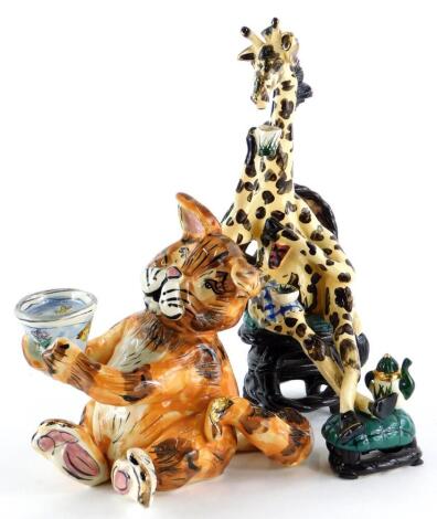 Two similar unusual pottery figures, depicting a giraffe drinking tea while seated and a cat begging with a bowl, 28cm high and 18cm high respectively.