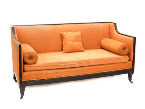 35 N/S - An early 19thC mahogany sofa, with a reeded show frame, upholstered in coral coloured fabric with upholstered cushions to each end, on turned fluted legs with castors, 180cm wide.