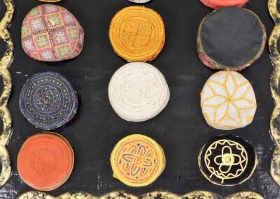 A collection of Kufi hats of various embroidered coloured design, (18), with a hand amde papier mache display panel, 94cm x 130cm. - 2